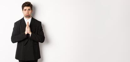 Miserable clingy guy need help, pouting silly and begging for something, asking for favour, standing against white background in black suit photo