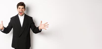 Portrait of pissed-off and frustrated businessman in suit, shouting angry and shaking hands, standing distressed against white background photo