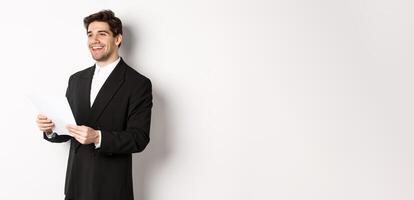 Image of handsome businessman in suit, holding documents and smiling, standing against white background photo