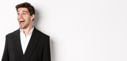 Close-up of handsome male entrepreneur in suit, looking left and smiling amazed, standing against white background photo