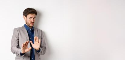 Stay away. Reluctant businessman step back with concerned disgusted face, raising hands to block bad offer, rejecting something awful, telling no and decline proposal, white background photo