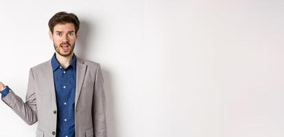 Whats wrong. Confused guy in suit cant understand, looking clueless with hand raised up, staring at camera questioned, standing on white background photo