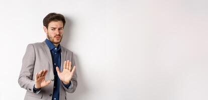 Stay away. Reluctant businessman step back with concerned disgusted face, raising hands to block bad offer, rejecting something awful, tilting from disgust, white background photo