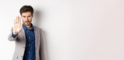 Hold right there. Serious businessman in suit stretch out hand and tell to stop, frowning and look confident, disapprove action, prohibit something bad, standing on white background photo