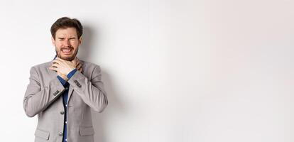 Crying man in suit holding hands on neck and look distressed, feel sick with sore throat, standing on white background photo