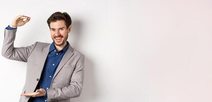 Successful businessman showing big size, shape large object and smiling pleased, standing on white background in suit photo