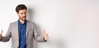 Excited handsome businessman showing long size thing, big object with stretch out hands, standing in suit on white background photo