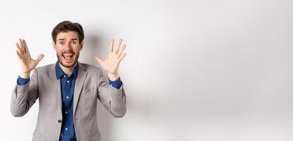 Businessman scream and shake hands in panic, look alarmed and anxious, shouting at camera, standing in suit on white background photo