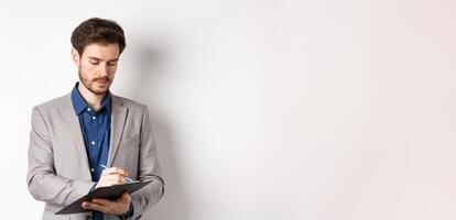 Office worker in suit writing on clipboard, taking notes on meeting, standing on white background photo