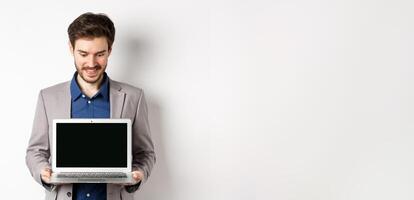 Handsome caucasian businessman in suit showing empty laptop screen, demonstrate promo, standing on white background photo