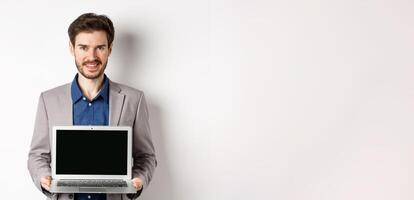 Handsome caucasian businessman in suit showing empty laptop screen, demonstrate promo, standing on white background photo