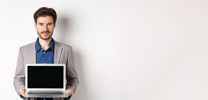 Handsome caucasian businessman in suit showing empty laptop screen, demonstrate promo, standing on white background photo