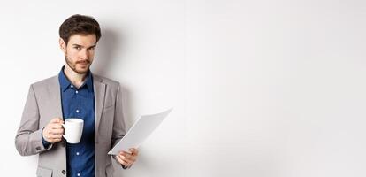 Businessman in suit reading documents papers and drinking coffee, smiling confident at camera, white background photo