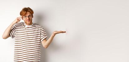 Are you stupid. Confused redhead guy in glasses shrugging, pointing at head and staring skeptical at camera, white background photo
