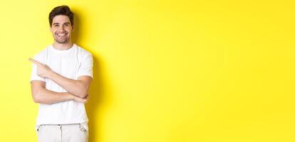 Handsome guy pointing left and smiling, showing advertisement on yellow copy space photo