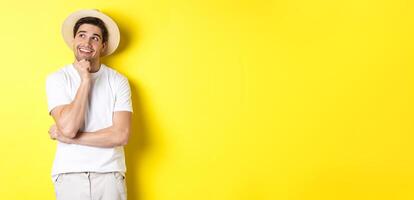 Young thoughtful man tourist imaging something, looking at upper left corner and smiling, thinking and standing over yellow background photo