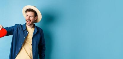 Happy smiling guy catching frisbee while playing with friends on summer vacation, standing in straw hat on blue background photo