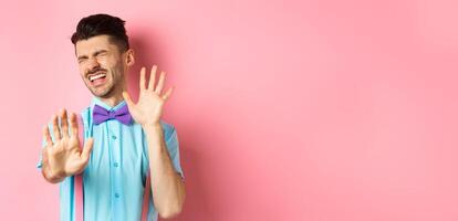 Crying guy asking to stop, raising hands up in defense, protecting himself from assault, standing over pink background photo