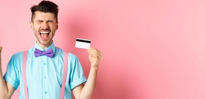E-commerce and shopping concept. Crying man showing empty smartphone screen and plastic credit card, feeling frustrated, standing on pink background photo