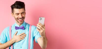 Image of handsome guy laughing during chat, having mobile conversation and chuckle from something funny, standing on pink background photo