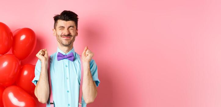 san valentin día concepto. alegre chico saltando desde emoción antes de romántico fecha, en pie cerca grande rojo corazones globos y celebrando, rosado antecedentes foto
