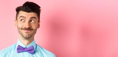 Close-up of handsome smiling guy with moustache, looking left at logo with pleased face, standing on pink background photo