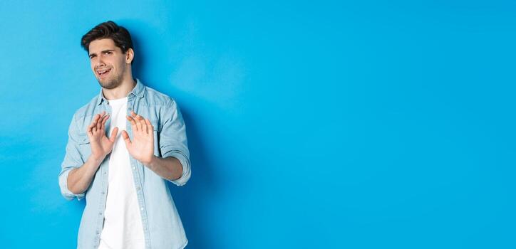 disgustado hombre negándose, diciendo No y encogerse desde alguna cosa desagradable, en pie terminado azul antecedentes foto