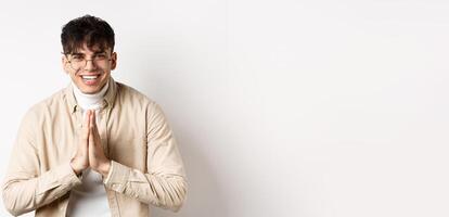 Handsome caucasian man say thank you, bowing with namaste gesture, looking grateful and smiling at camera, standing on white background photo