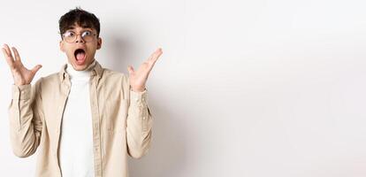 Scared young man in panic, screaming and looking axious, jumping startled and shocked, shaking hands nervously, standing on white background photo
