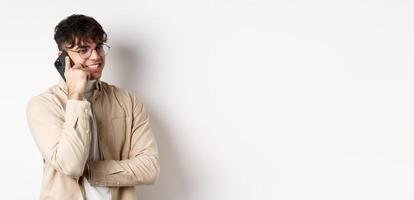 Real people concept. Handsome modern man talking on mobile phone, look aside and holding smartphone near ear, standing on white background photo