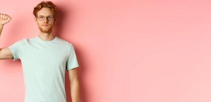 Confident redhead man standing united with black lives matter movemet, showing raised fist and looking serious at camera, protesting and being an activist, standing over pink background photo