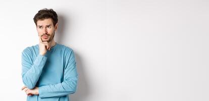 Young bearded man looking pensive and frowning, thinking about problem or trouble, standing worried against white background photo