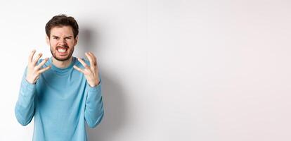Angry caucasian man shaking hands and grimacing, looking with mad face, express hatred against white background photo
