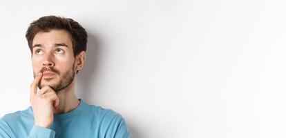 Face of young caucasian man looking up pensive, making choice or thinking, pondering while standing over white background photo
