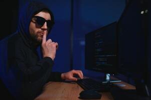 hacker sitting at desk in dark atmosphere. A computer programmer or hacker. Anonymous computer hacker. photo