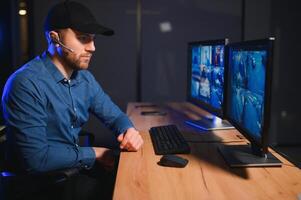 Rear view of security system operator looking at CCTV footage at desk in office photo