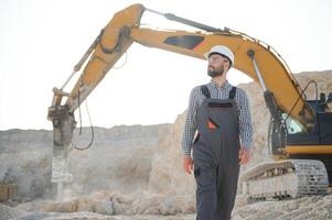 A worker in a helmet stands on the background of an excavator in a quarry photo