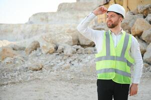 A worker in a helmet stands on the background of an excavator in a quarry photo