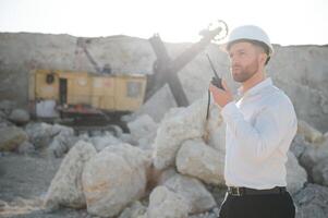 A worker in a helmet stands on the background of an excavator in a quarry photo