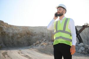 A worker in a helmet stands on the background of an excavator in a quarry photo