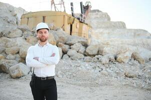 A worker in a helmet stands on the background of an excavator in a quarry photo
