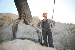 A worker in a helmet stands on the background of an excavator in a quarry photo