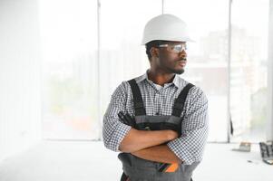 retrato de hermoso joven africano americano masculino constructor en difícil sombrero, trabajando a construcción sitio foto