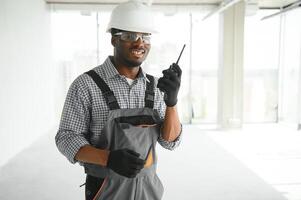 constructor en casco es en pie en frente de el construcción sitio, hablando por walkie película sonora controlar y comunicar con trabajador foto