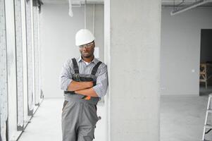 retrato de hermoso joven africano americano masculino constructor en difícil sombrero, trabajando a construcción sitio foto
