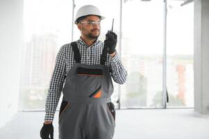joven mezclado carrera supervisor instruyendo trabajadores utilizando walkie-talkie a construcción sitio. foto