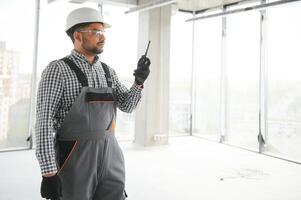 joven mezclado carrera supervisor instruyendo trabajadores utilizando walkie-talkie a construcción sitio. foto