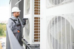 Indian Repairman in uniform installing the outside unit of air conditioner photo