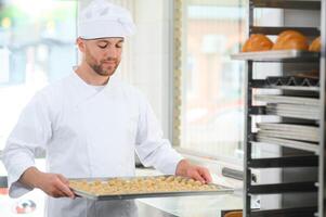Young Caucasian worker in work wear holding tray with cookies photo