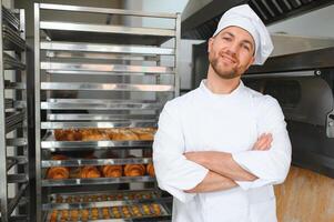 Portrait of handsome baker at the bakery with breads and oven on the background photo